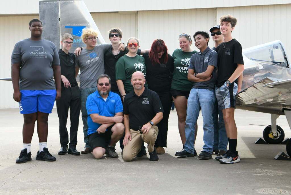 Group of people standing in front of a silver airplane, smiling and posing for a photo.