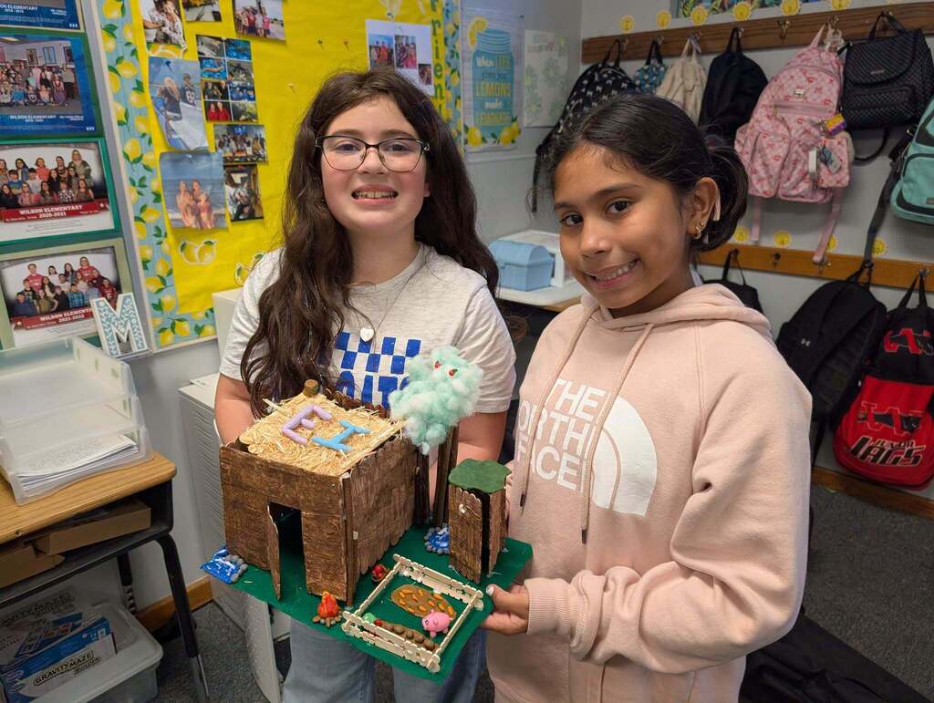 Two girls smiling, one holding a model igloo with a candy roof and the other holding the igloo's base.