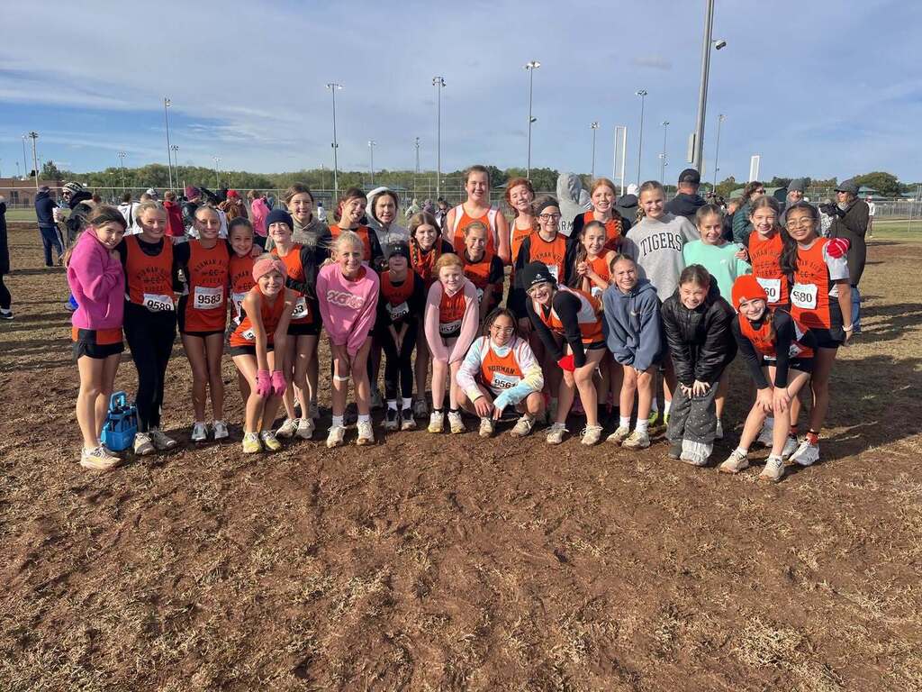 Group of people in sports gear on dirt field, some wearing numbered bibs, posing for a photo.
