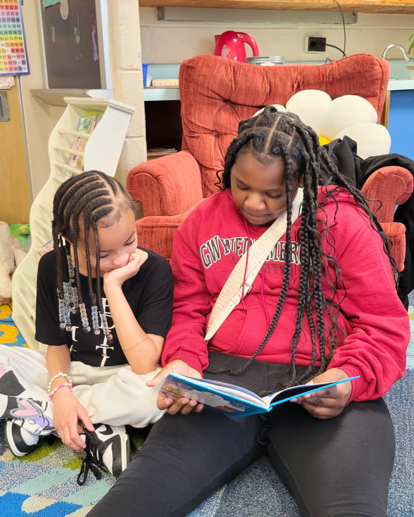 Two students sitting in a classroom reading a book together