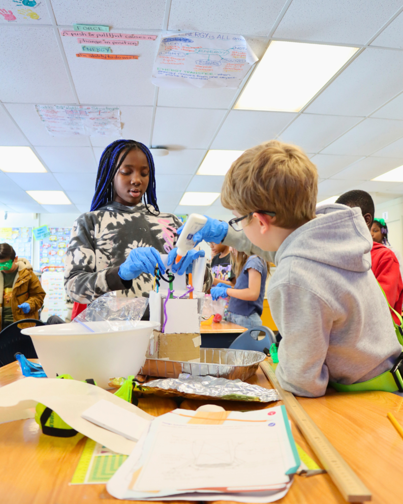 Students working on a hands-on science experiment with various materials and containers in a classroom.