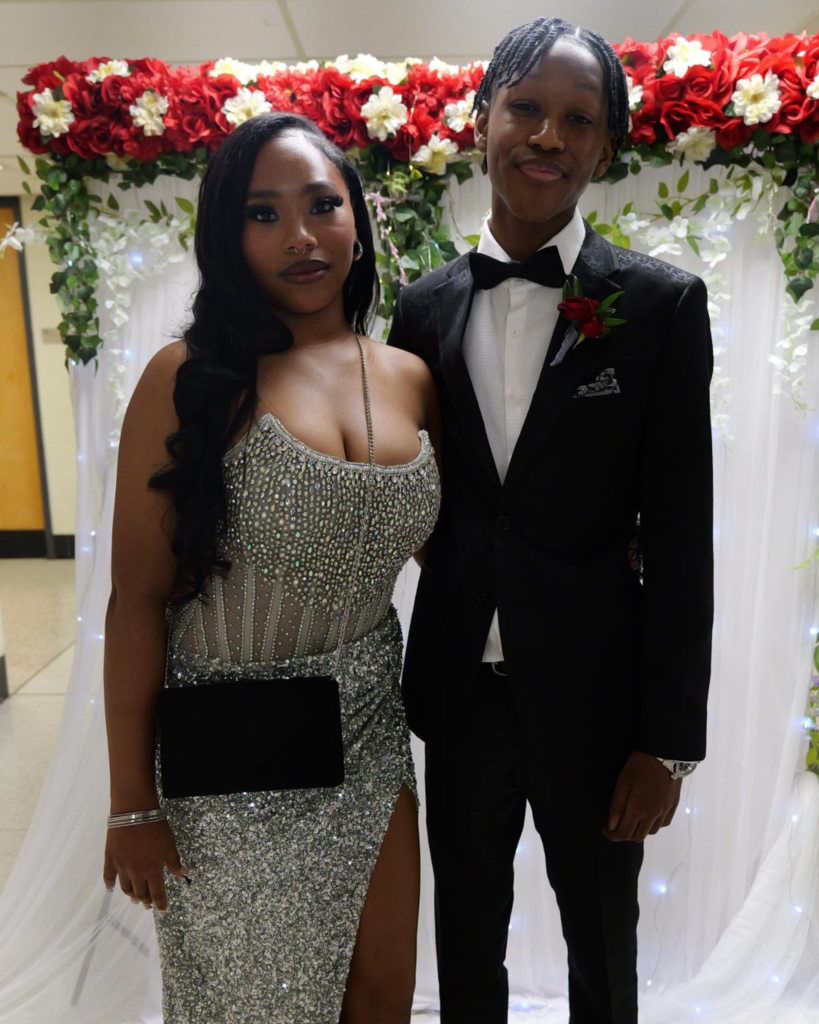 Two students at the junior prom posing for photo in front of white backdrop decorated with flowers