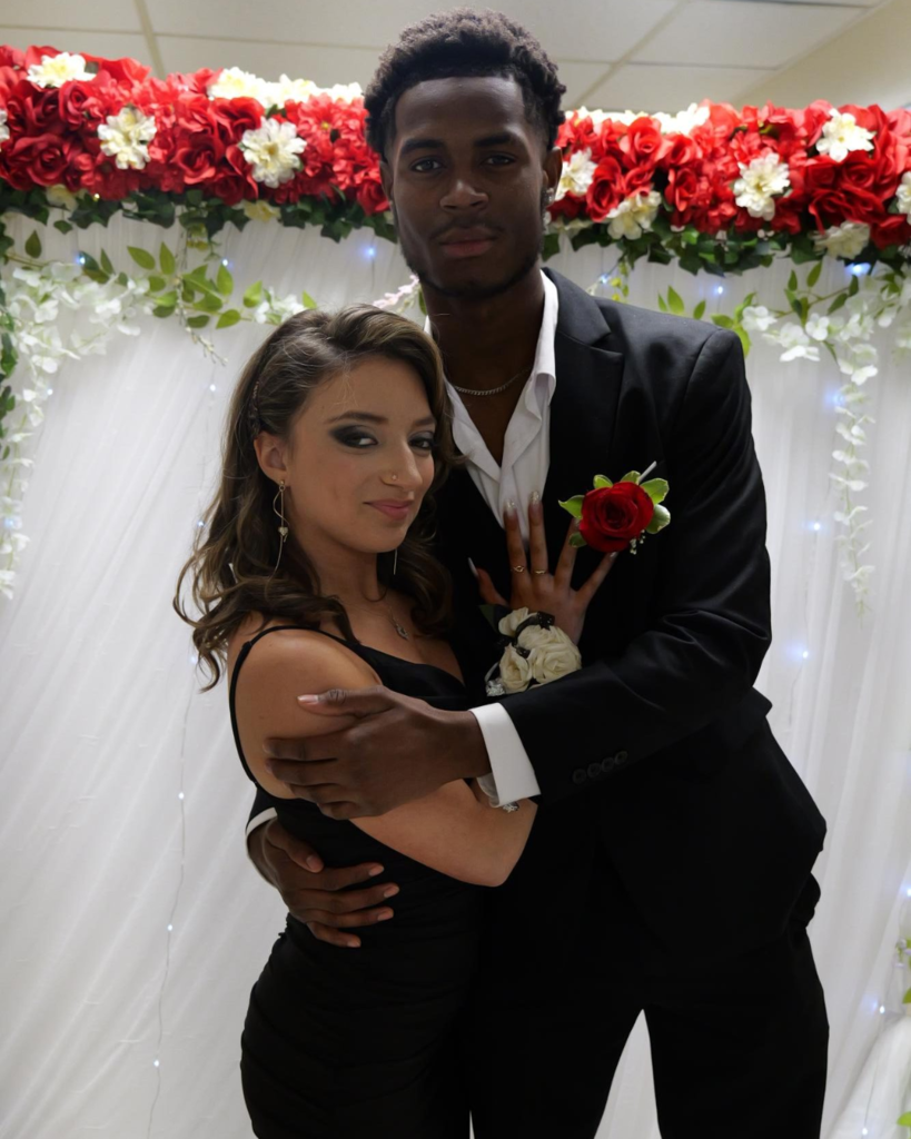 Two students at the junior prom posing for photo in front of white backdrop decorated with flowers