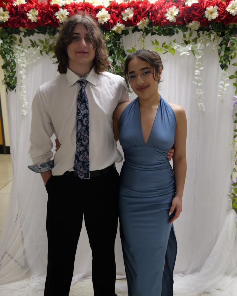 Two students at the junior prom posing for photo in front of white backdrop decorated with flowers