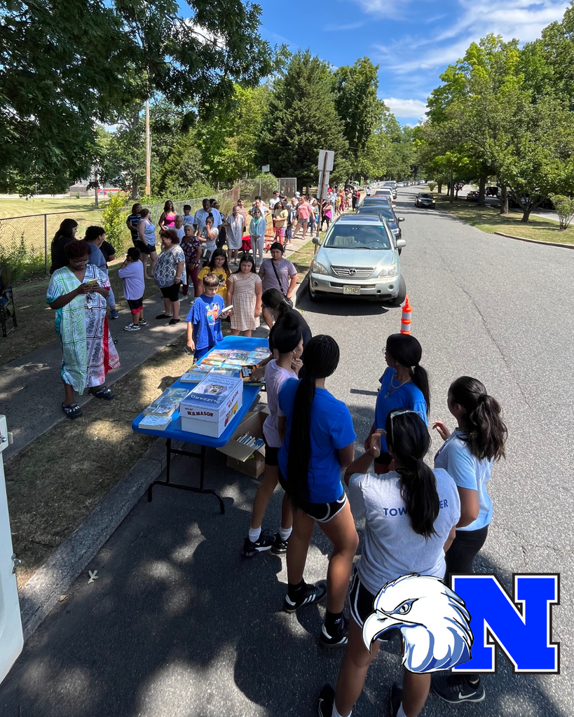 Families lined up for meal distribution with student volunteers standing near the free books table