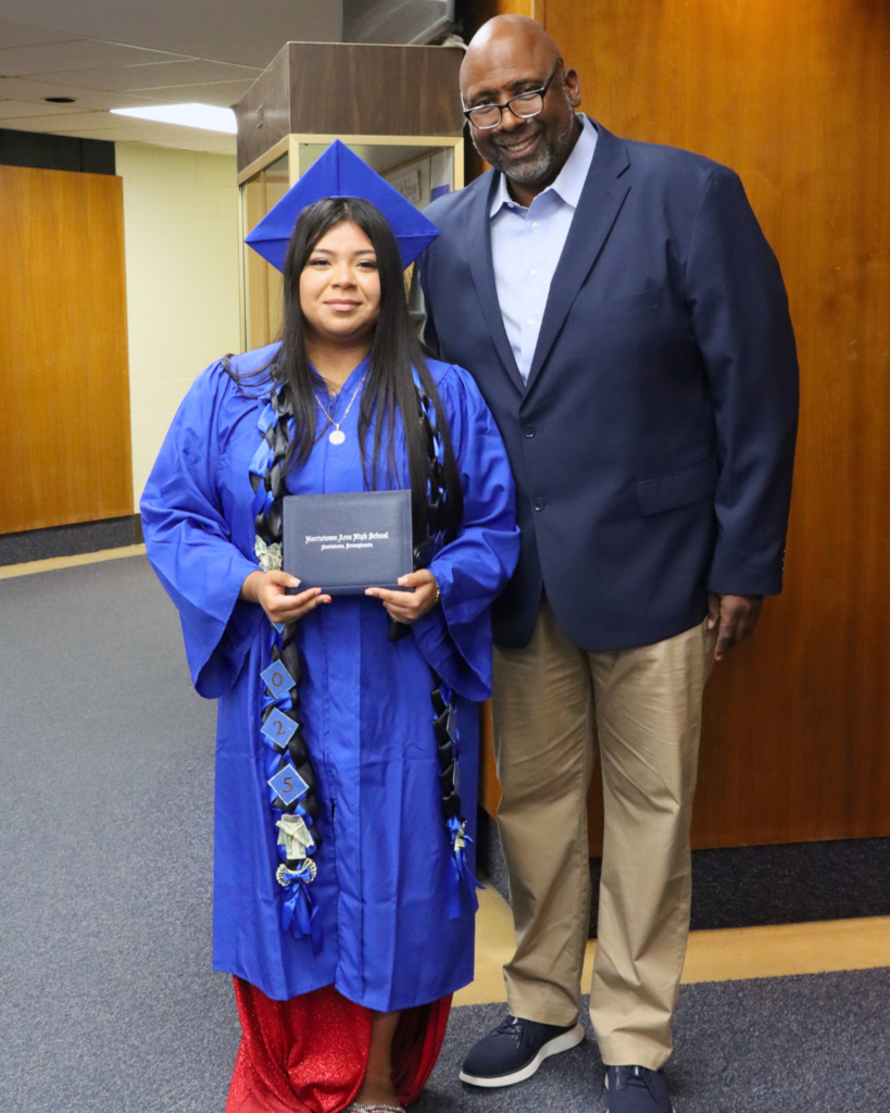 Graduate in blue cap and gown stands with Dr. McGriff, principal while holding diploma.