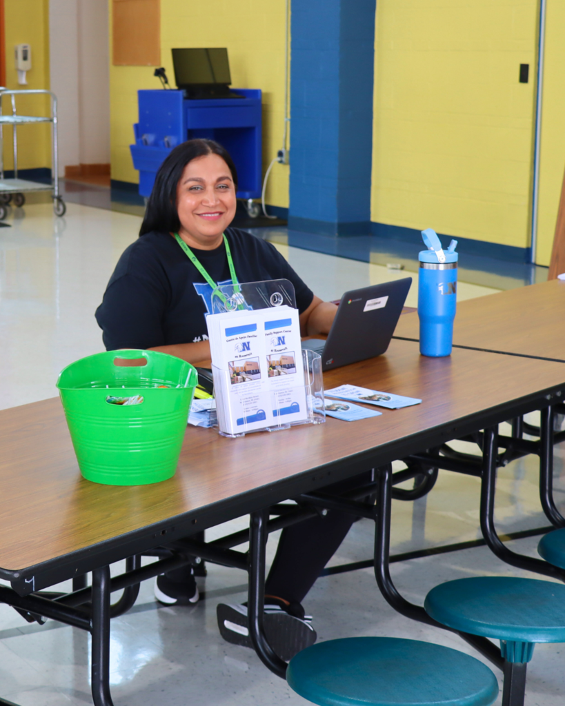 NASD Staff member smiles for a photo while sitting at a table with brochures displayed.
