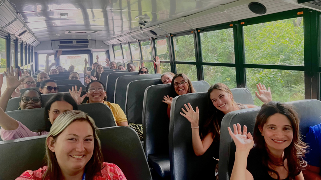 New teachers waving for a photo while on the bus.