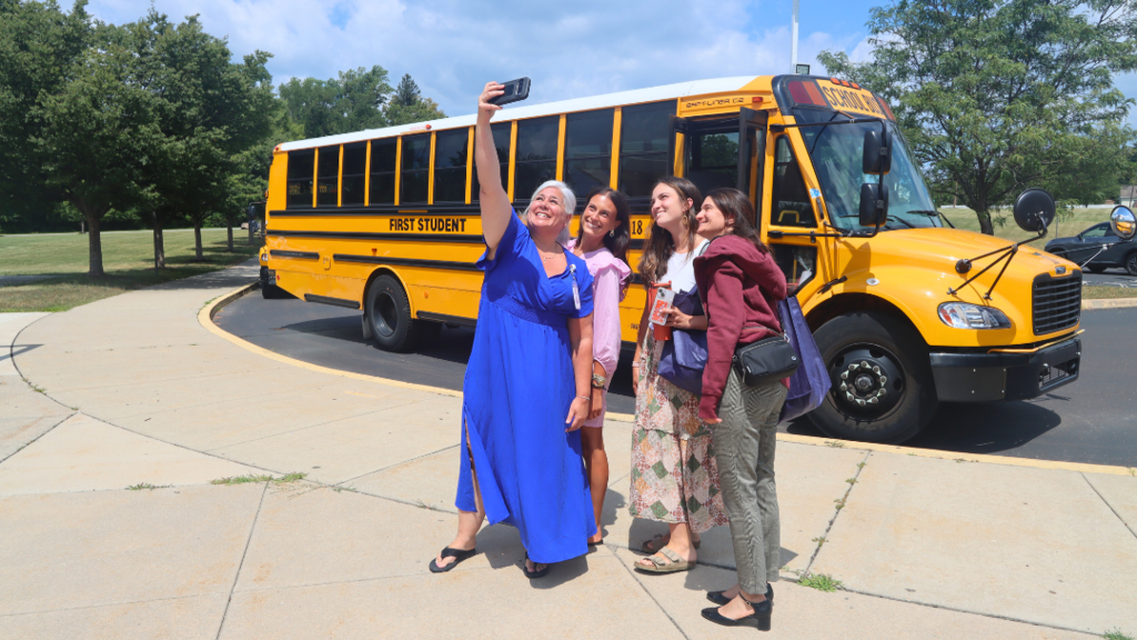 Four new teachers taking a selfie in front of the tour bus.