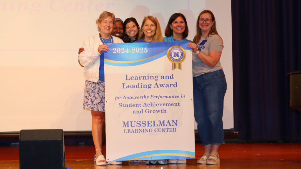 Musselman Learning Center team poses for photo on stage with their Learning and Leading award banner.