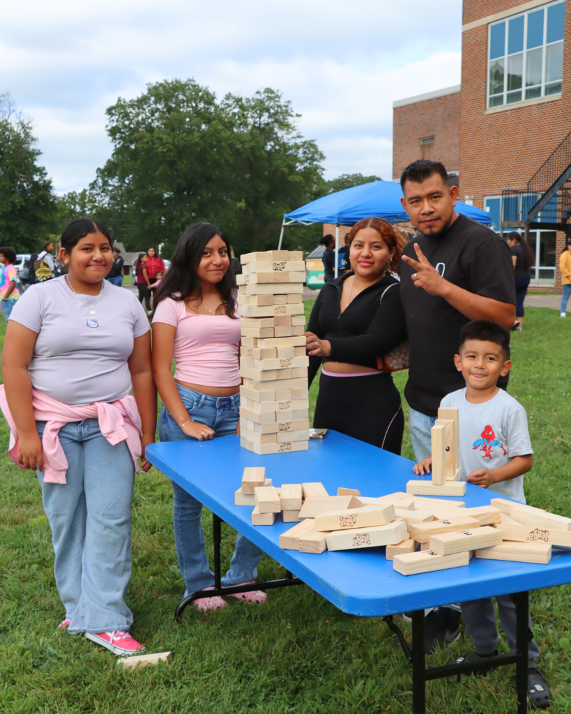 Family poses for photo at table set up with jumbo jenga blocks at back to school event.