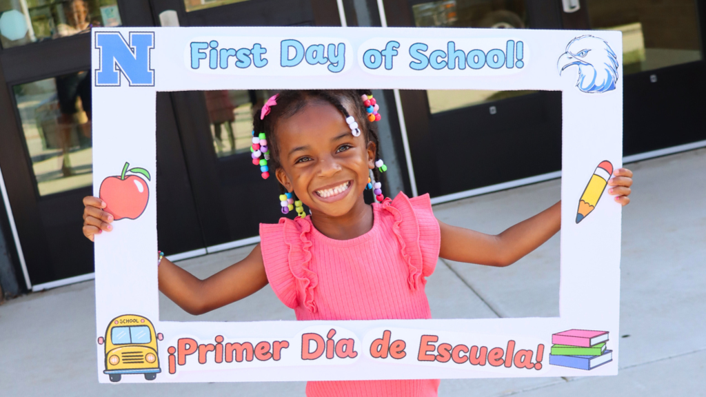Young student smiling for a photo holding a first day of school poster frame.