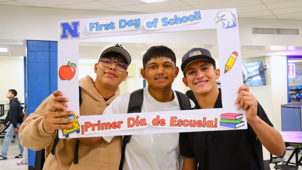 Three students pose for photo with first day of school poster frame.