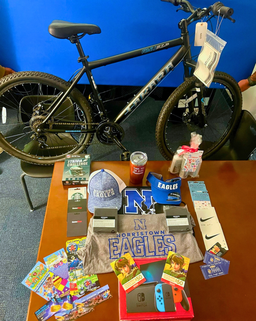 Potential prizes displayed across a table including Norristown t-shirt, gift cards, a bike, Nitendo Switch, and more.