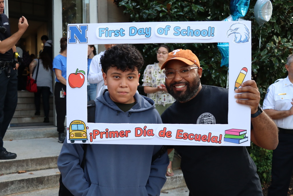 Two students in a photo booth square that says "First Day of School". More information in caption