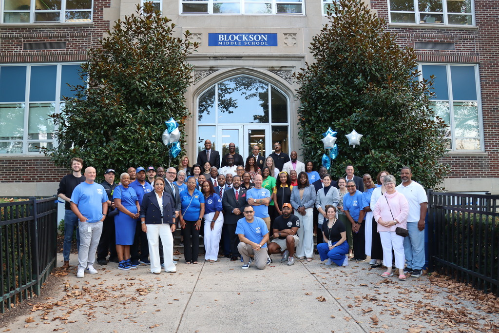 Group photo of teachers and VIP community members in front of Blockson Middle School. More information in caption.