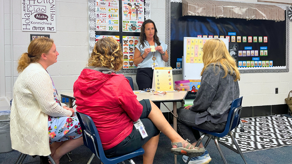 Three educators sitting at a table while another educator is presenting to them.
