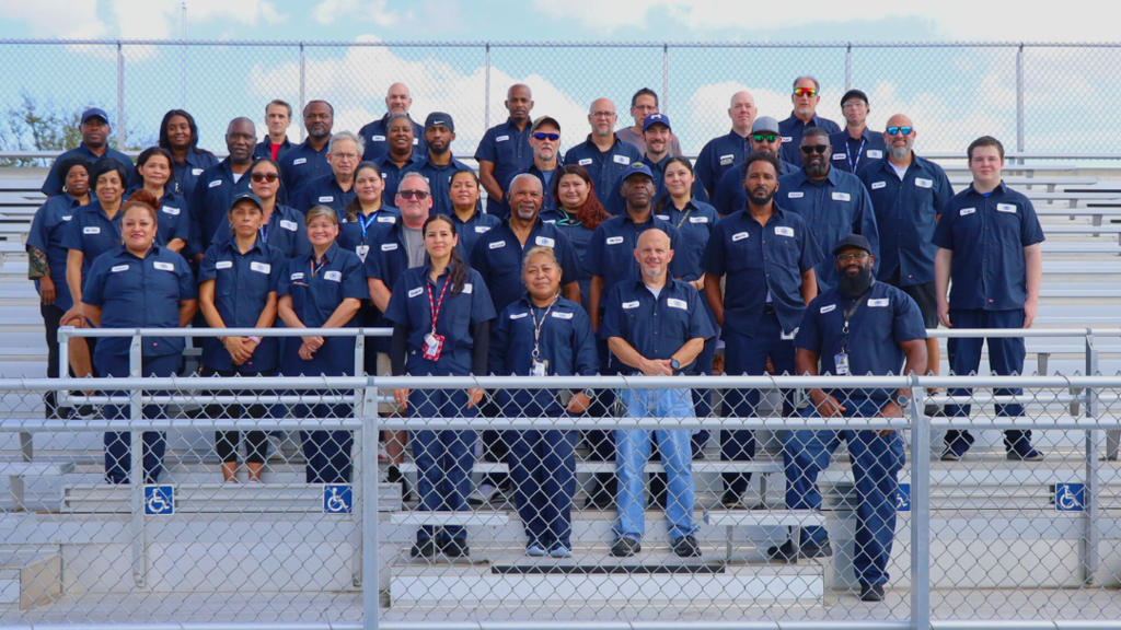 Custodial staff pose for large group photo on bleachers. 