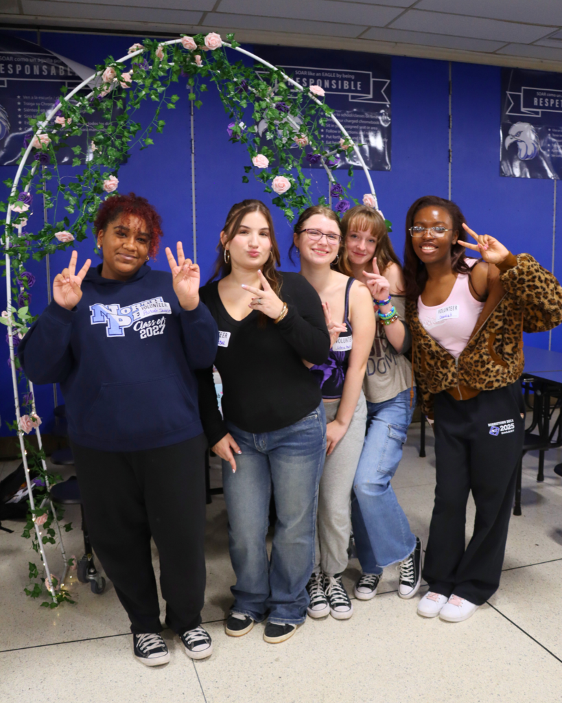 Drama club students pose for phot in front of flower backdrop.