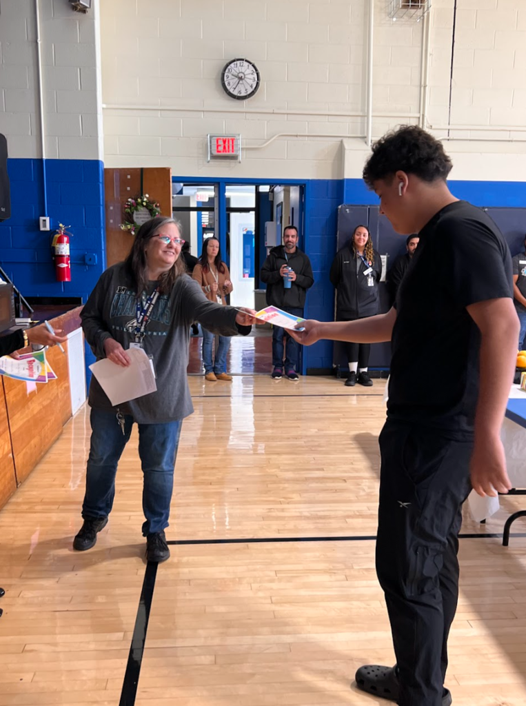 A teacher is handing a certificate to a student who is being recognized as a star student of the month. 