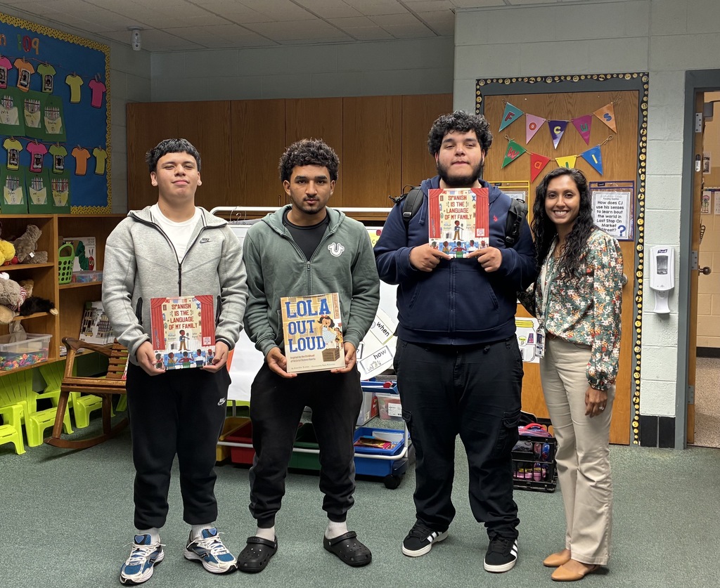 Three students and an advisor are posing with books after reading to the elementary school students.