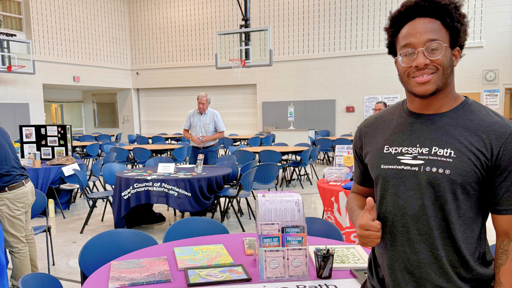 Representative from community organization poses for a photo with their table set up with information and resources.