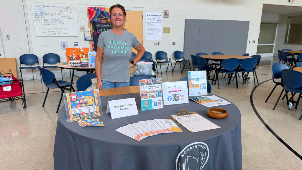Representative from community organization poses for a photo with their table set up with information and resources.