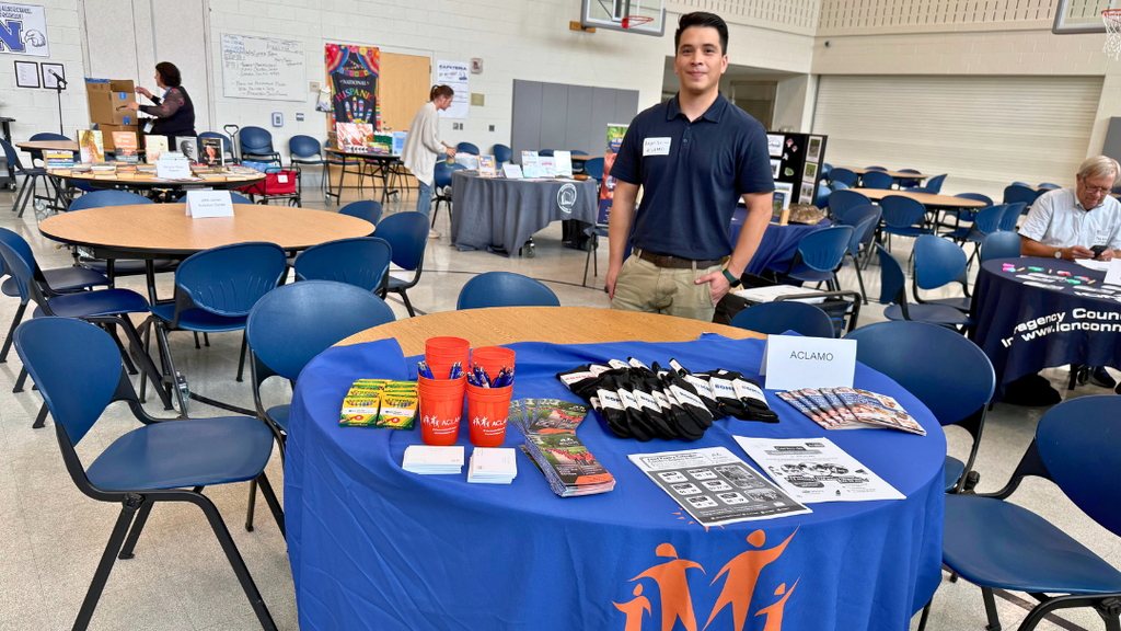 Representative from community organization poses for a photo with their table set up with information and resources.