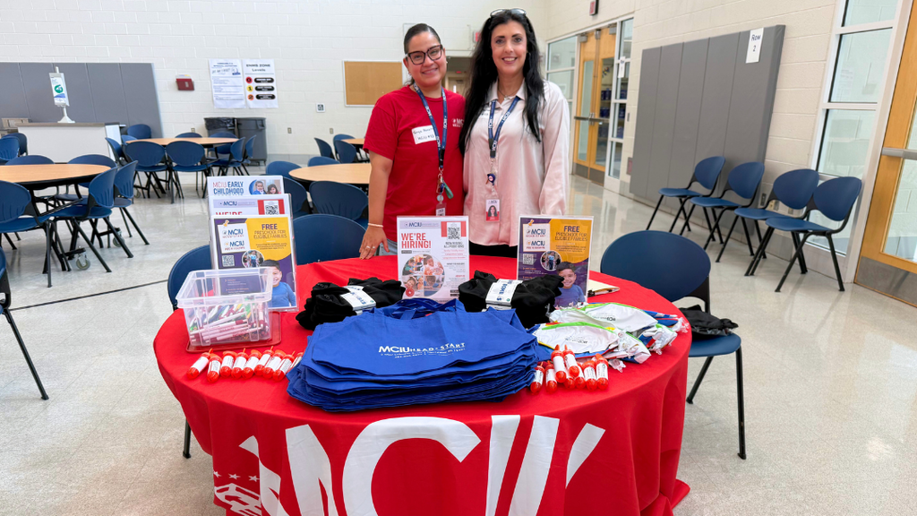 Two representatives from community organization pose for a photo with their table set up with information and resources.