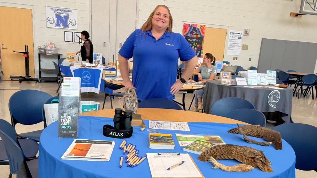 Representative from community organization poses for a photo with their table set up with information and resources.