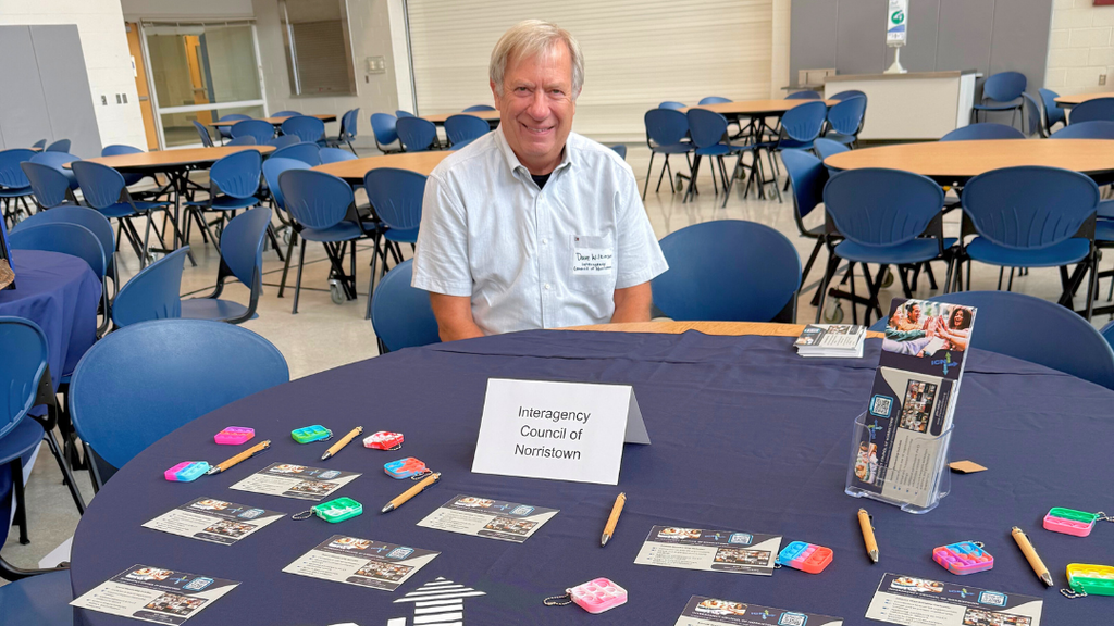 Representative from community organization poses for a photo with their table set up with information and resources.
