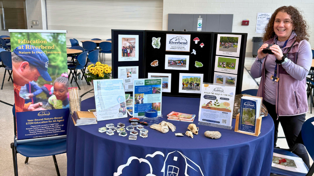 Representative from community organization poses for a photo with their table set up with information and resources.