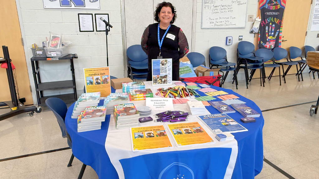 Representative from community organization poses for a photo with their table set up with information and resources.