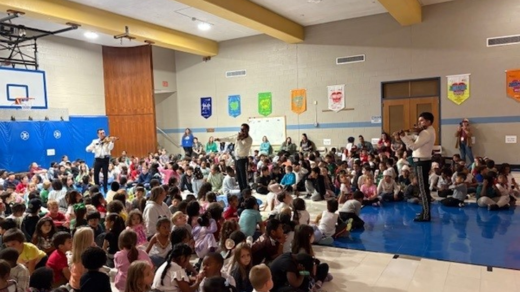 Students sitting on the gym floor watching mariachi band perform.