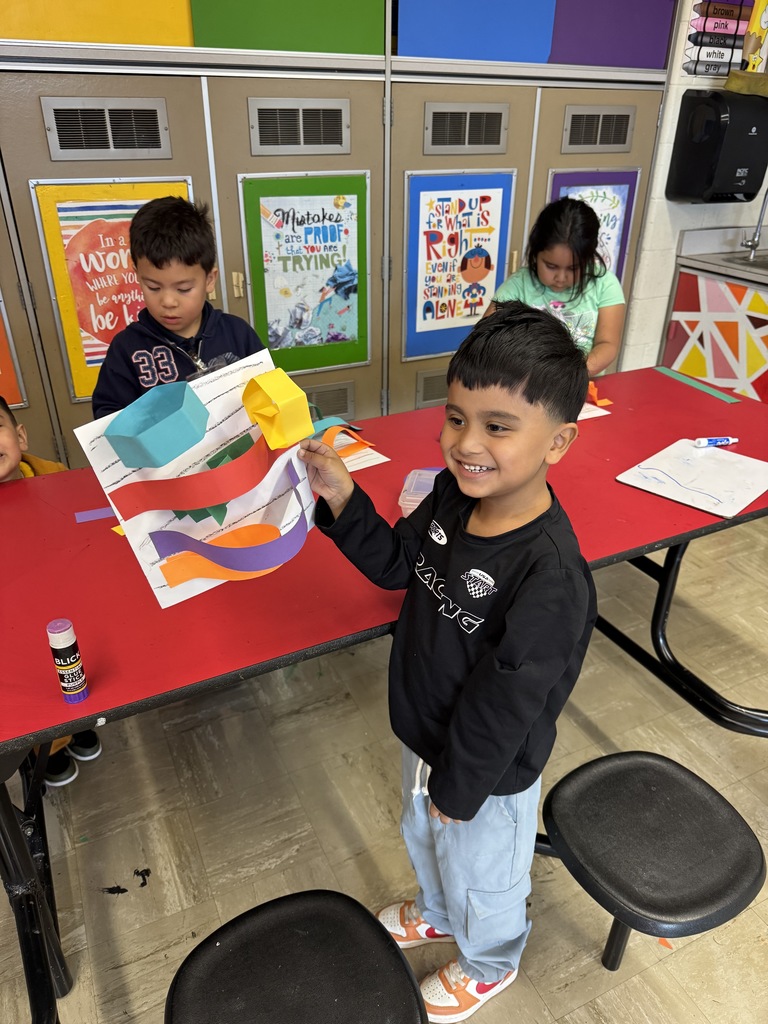 A kindergartner shows his rainbow paper line sculpture.
