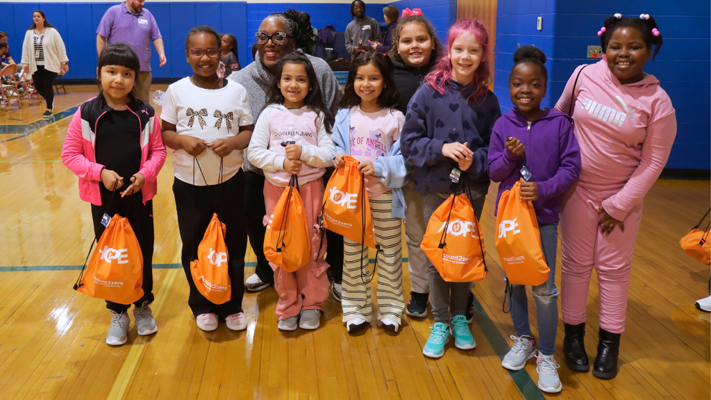 Group of students holding their bags with their new shoes pose for a photo with Principal Dr. Harper.