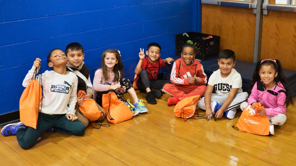 Group of students sitting on the floor pose for photo with their new shoes.