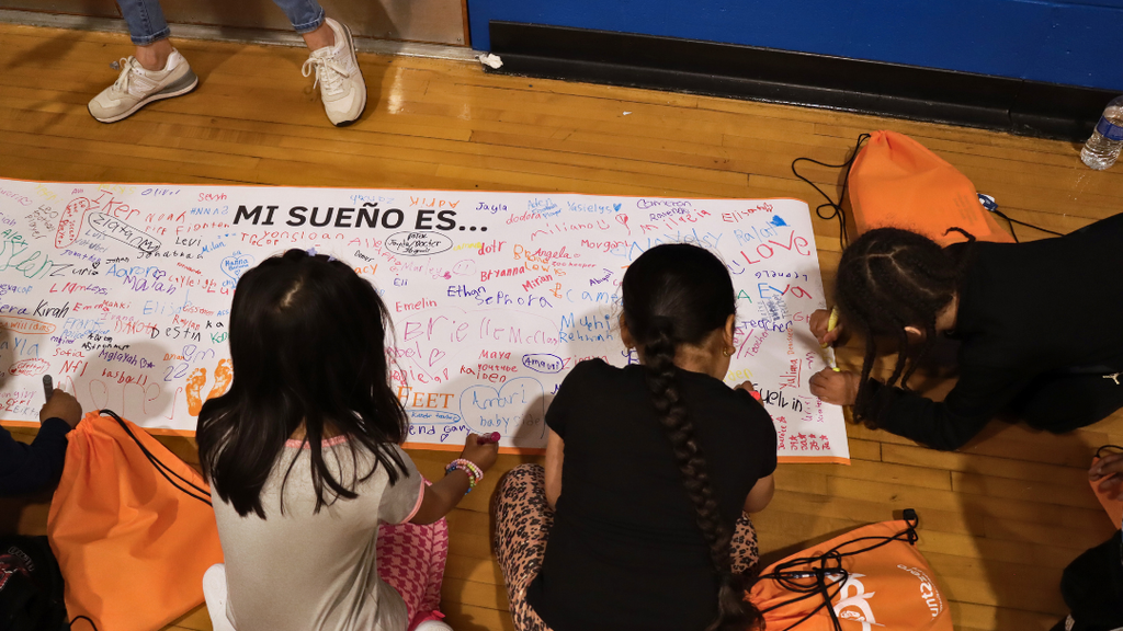 Students signing their name on a poster that has text "MI SUEÑO ES..."