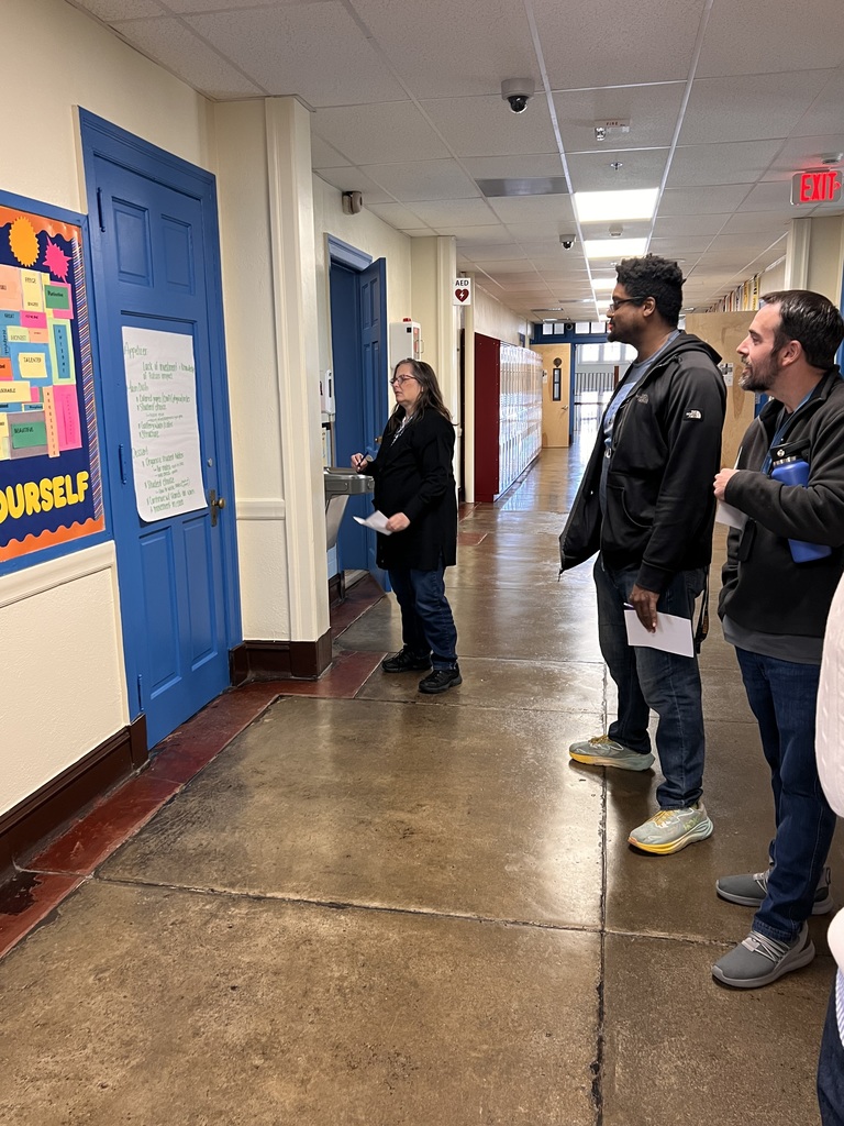 Three teachers are looking at a poster in the hallway as a part of a gallery walk