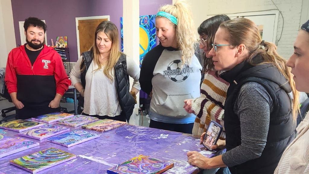 Teachers looking at all of the canvases displayed on a table.