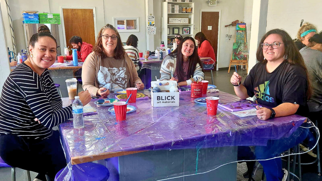 Teachers working on paintings at a table smile for a photo.