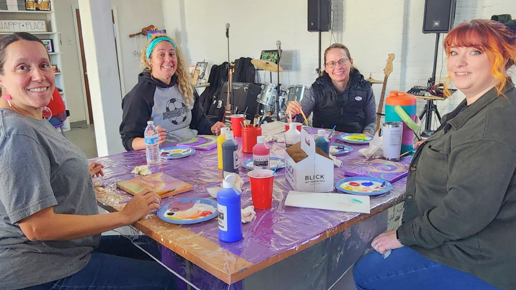 Teachers working on paintings at a table smile for a photo.