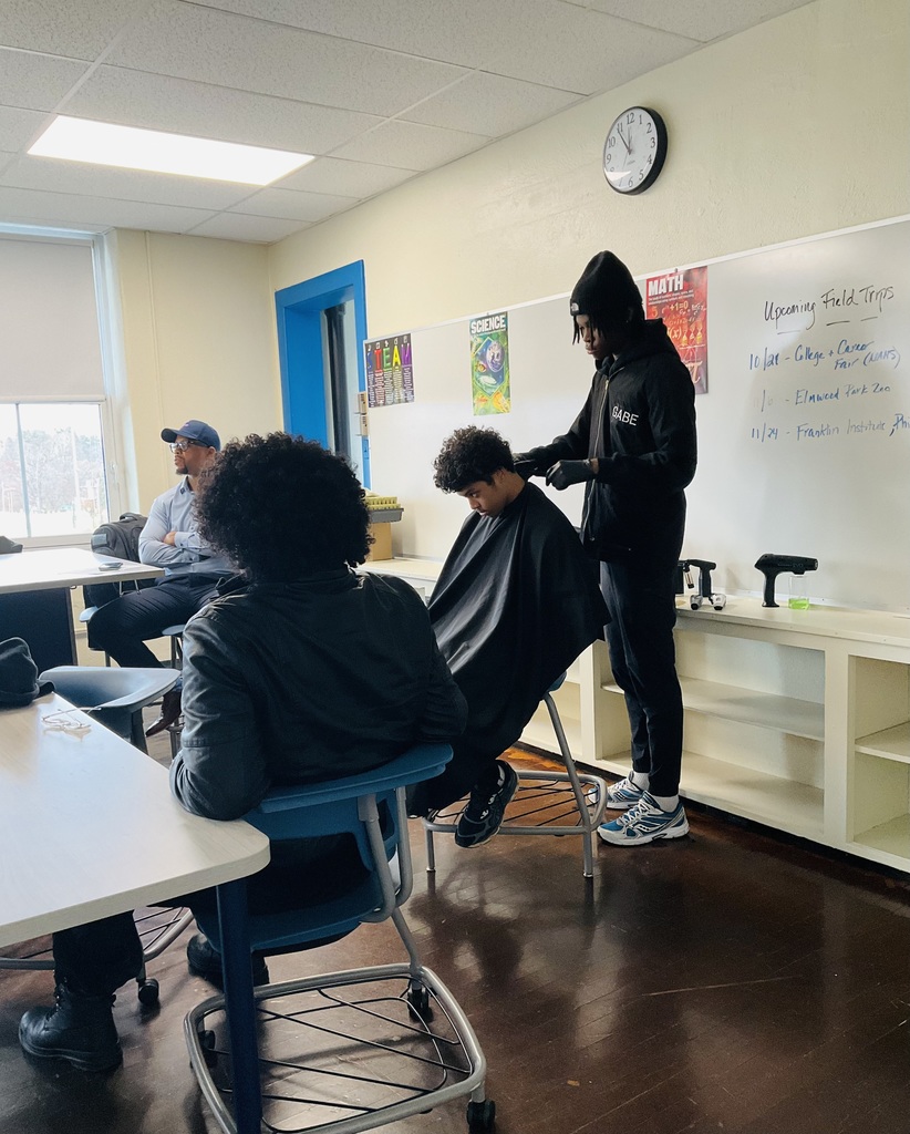 A student is getting his hair cut while a presenter is talking