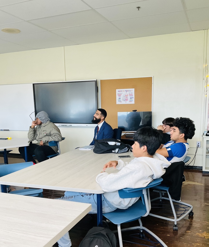 Students are actively listening to the presenter talk. A counselor is also with the students listening.