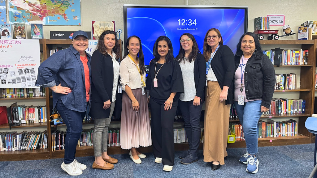 Elementary Community Liaisons pose for photo standing in front of bookshelf and screen.