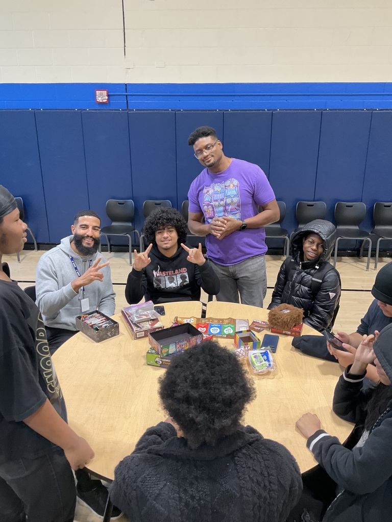 Students and staff are posing in a picture together at a table in the cafeteria
