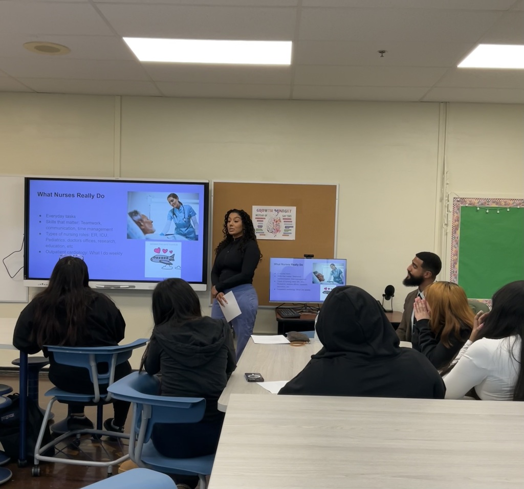 A nurse is in the front of the classrooom giving a presentation about nursing to a group of students.