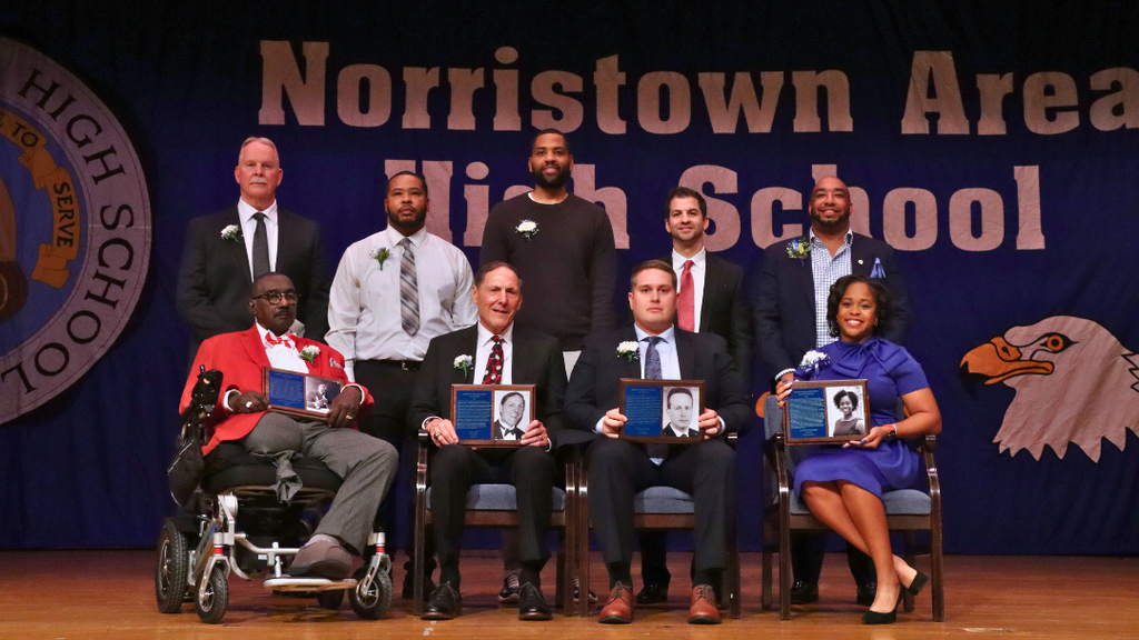 Hall of Campions and Hall of Fame Inductees on stage pose for group photo holding their plaques. 