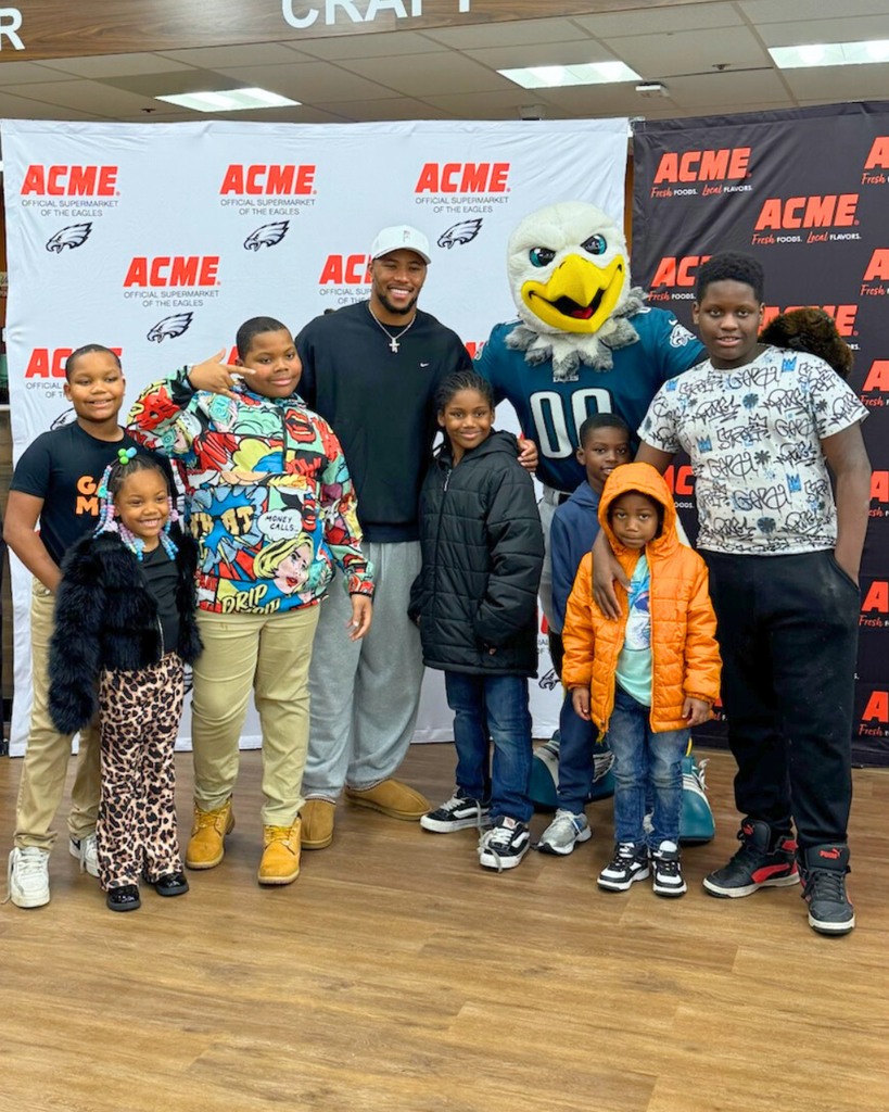Students pose for photo with Saquon Barkley in front of ACME backdrop.