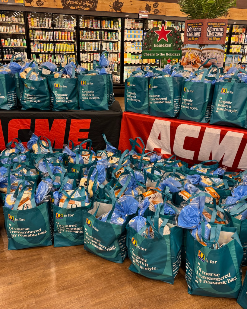Reusable bags packed with Thanksgiving meals displayed on tables and on the floor in front of the tables. 
